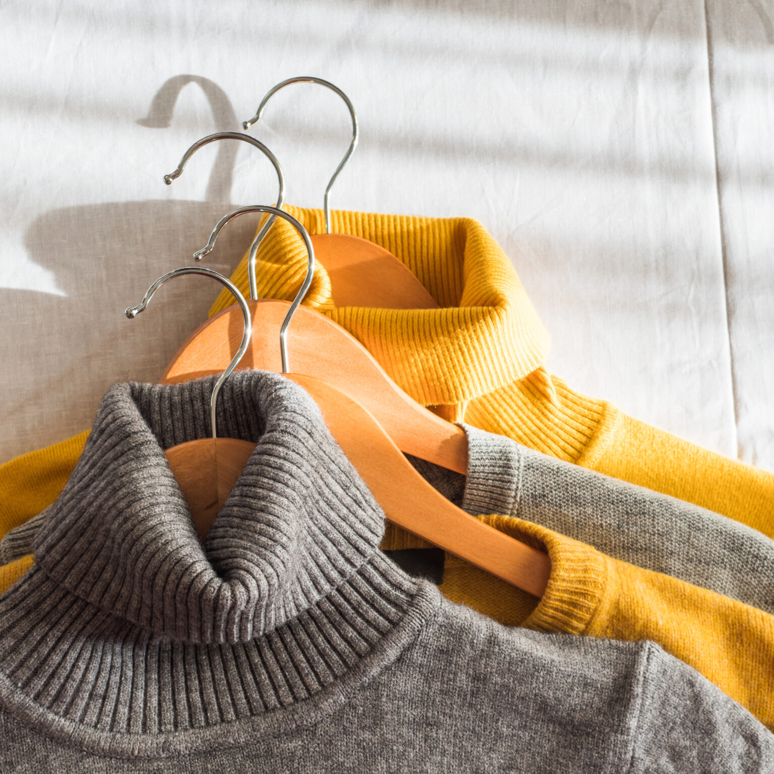 Yellow illuminated color and gray winter sweaters on wooden hangers. Trendy fashion autumn warm and cozy clothes. Square